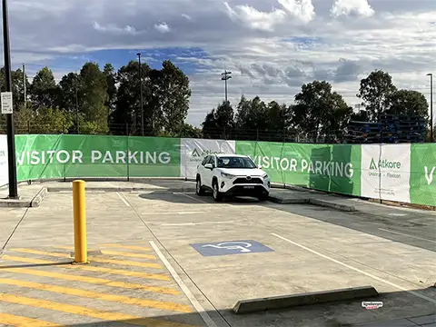Ground-level view of shade cloth signage on a curved fence with a parked car