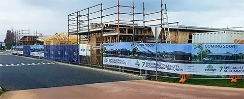 Left side of the construction site with multiple fence wraps and boards, signs and logos.