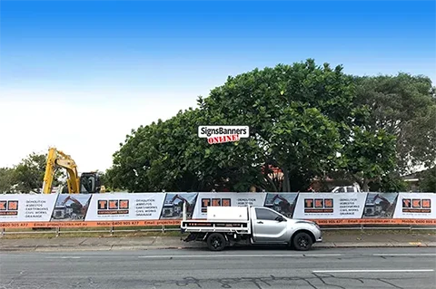 Image shows full coverage from let to right of temporary fencing with banners attached of the construction site with a vehicle parked