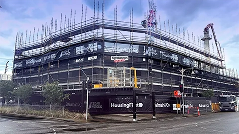 Multi storey housing building in construction with banners fitted on the outside. Super strong site maxi mesh and printed shade cloth for the large construction of a building during different phases of elevation. The wraps are gradually affixed to the building as it grows.