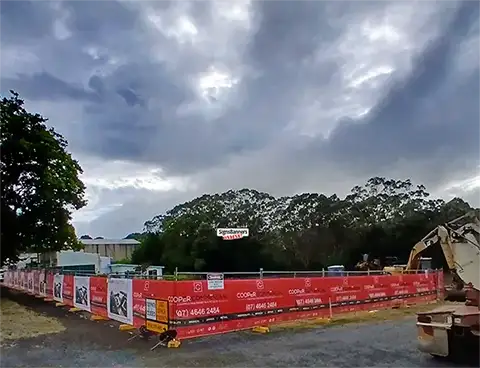 This customer image of a building site with fence installation still standing after a severe stormincludes a brightly colored red fence mesh back with the business branding and logos.