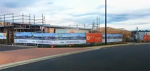 This image of a typical construction site includes fence cover wrap, safety signs, site boards and mandatory OHS boards with the construction in the background.